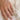 Hand wearing a gold ring with a round, bezel set diamond on a light fabric background