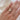 Hand wearing a gold, solitaire ring paired with a curved, five diamond band on a white fabric background
