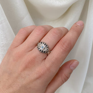 hand with sterling silver ring on middle finger in front of white backdrop. Eyeball ring with pale blue sapphire.