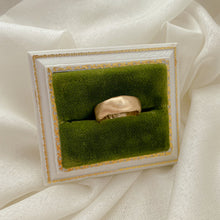 Load image into Gallery viewer, A recycled 14k gold wedding band displayed on a green cushioned platform with a gold trim, set against a white fabric background.
