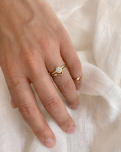 Load image into Gallery viewer, Hand wearing a gold ring with a round, bezel set diamond on a light fabric background