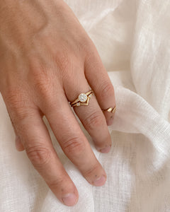 Hand wearing a gold ring with a round, bezel set diamond on a light fabric background