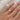 Gold ring with a round diamond in a bezel setting, on a hand against a light fabric background
