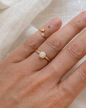 Load image into Gallery viewer, Gold ring with a round diamond in a bezel setting, on a hand against a light fabric background