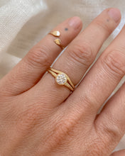 Load image into Gallery viewer, A round diamond, solitaire, gold ring on a hand against a neutral background. The solitaire is paired with a slightly curved, thin gold band.