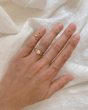 Load image into Gallery viewer, Hand wearing a two ring set; one round diamond solitaire ring and the other, a thin, curved gold band on a white fabric background. 