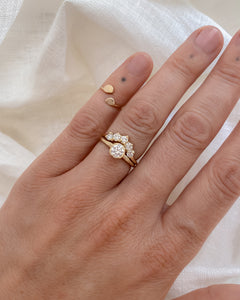 Hand wearing a gold, solitaire ring paired with a curved, five diamond band on a white fabric background
