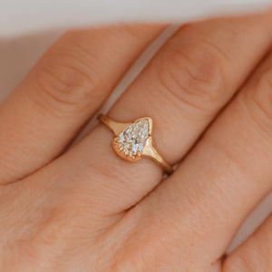 A pear-shaped white diamond ring set in a 14k gold band, displayed on a person's finger.