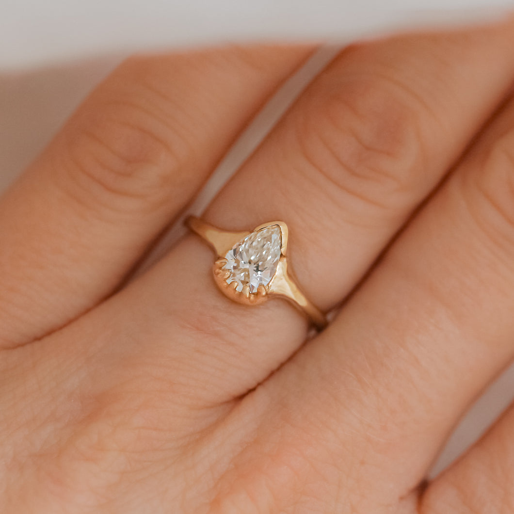 A pear-shaped white diamond ring set in a 14k gold band, displayed on a person's finger.
