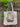 Canvas tote with a picture of cat lying on a fainting couch with plants hanging on the wall behind it.