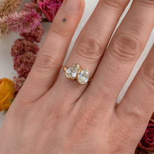 Load image into Gallery viewer, Person wearing toi et moi style engagement ring with one pear shaped diamond and one oval shaped diamond, side by side in melty setting. 