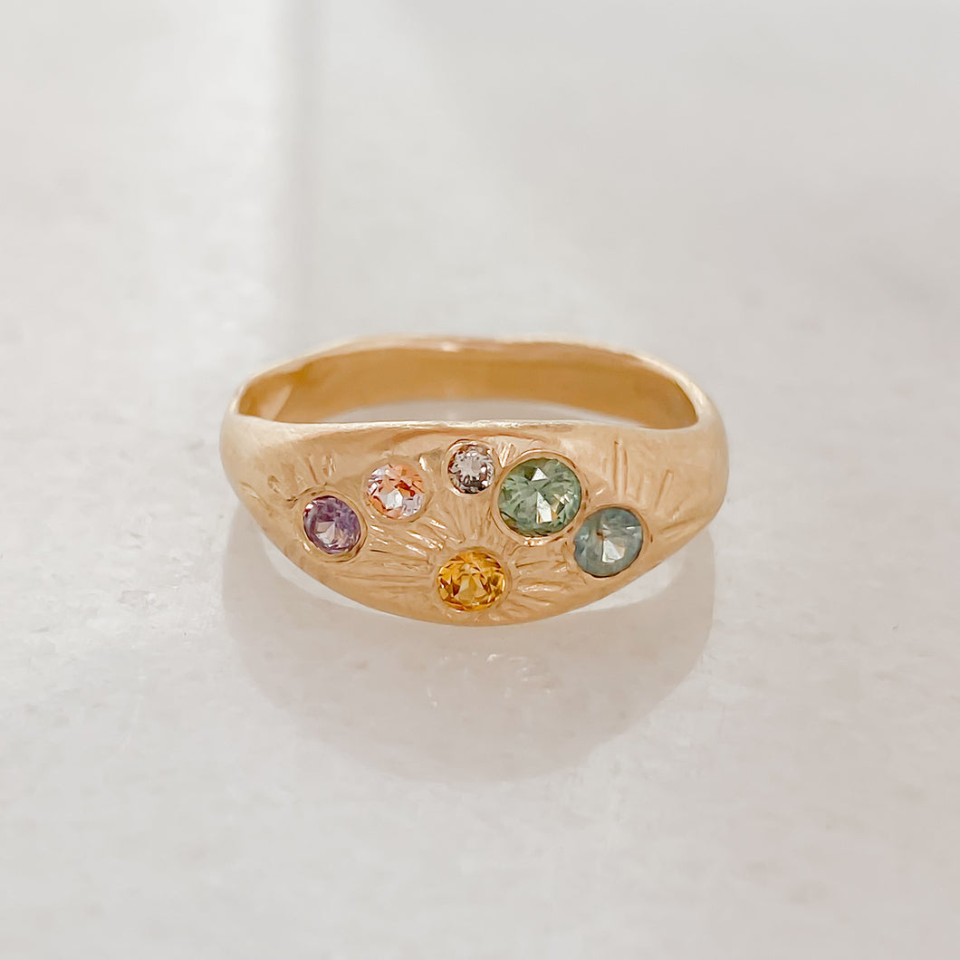 A gold signet ring with multiple colored gemstones set around its circumference.