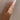 Hand wearing a halo ring with colorful gemstones against a neutral background