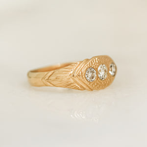 A gold ring with three white diamonds set in a hand-engraved pattern on the band.