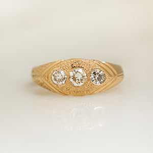 A gold ring with three white diamonds set in a hand-engraved pattern on the band.