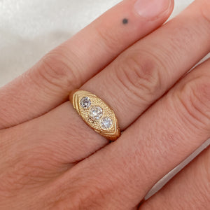 Woman wearing gold ring with three white diamonds set in a hand-engraved pattern on the band.