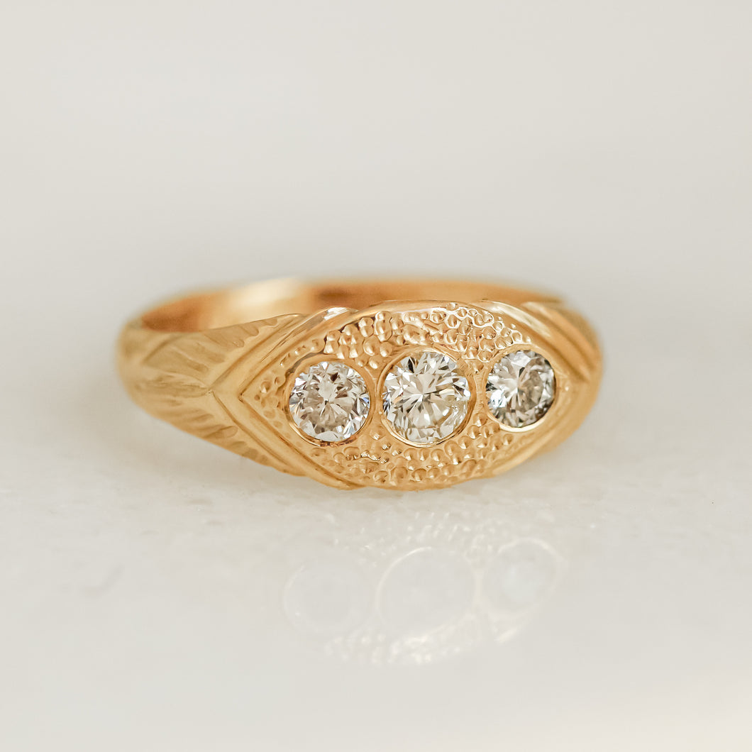 A gold ring with three white diamonds set in a hand-engraved pattern on the band.
