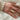 A hand wearing a white sweater, displaying a gold signet ring with a smiley face design on the ring finger.