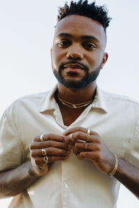man-leaning-over-camera-wearing-rings-and-necklaces
