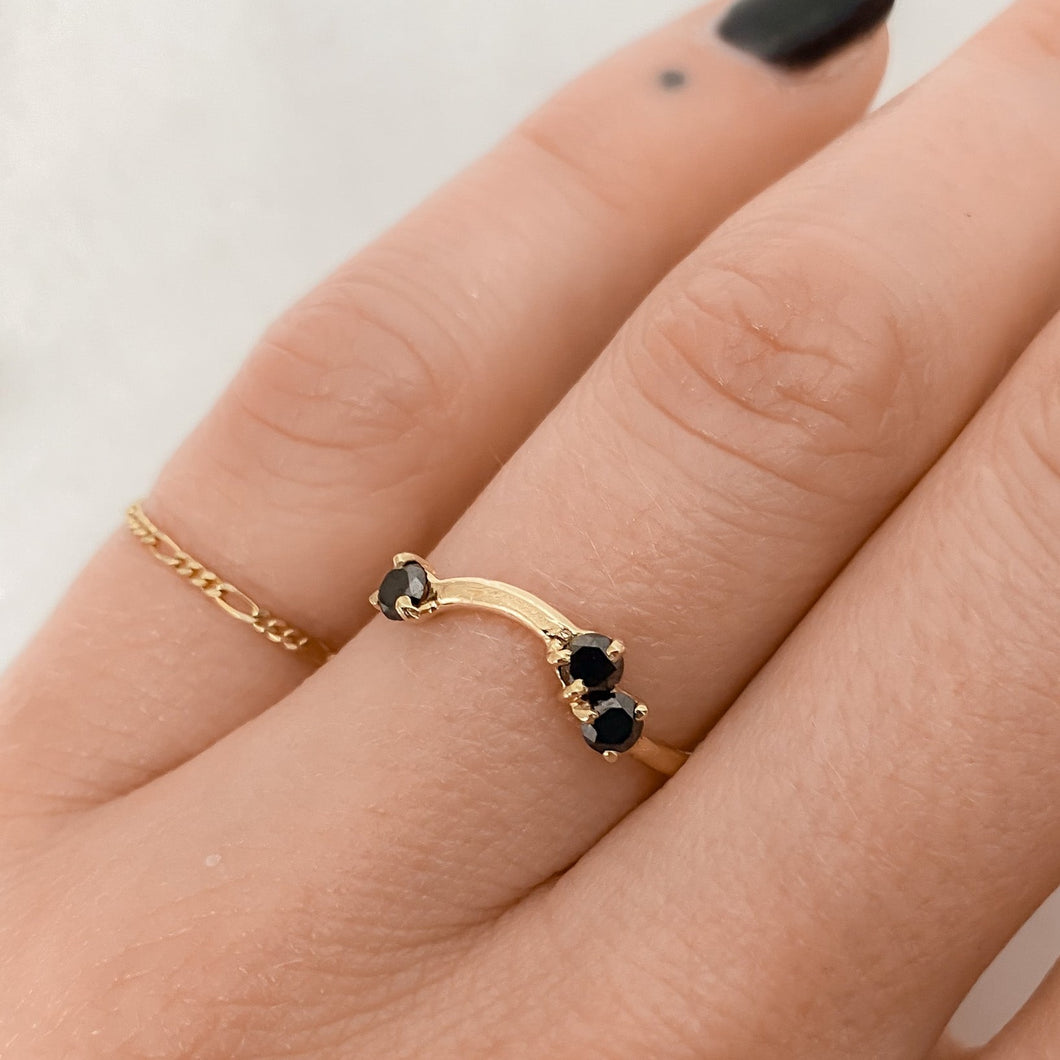 A handcrafted 14k gold band ring with three black, brilliant cut round diamonds set on it, worn on a person's finger.