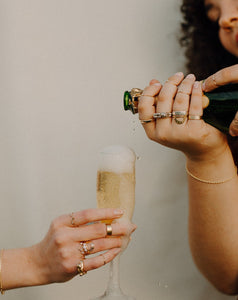 woman-pouring-overflowing-champage-into-a-flute-held-by-hand-wearing-lots-of-rings