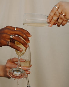 people-wearing-stacks-of-gold-and-silver-rings-pouring-champagne-into-flutes