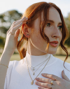 red-head-in-white-ribbed-sweater-wearing-layered-necklaces-and-stacked-rings