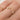 A person's hand wearing a pointed gold band ring with two white diamonds set on it.