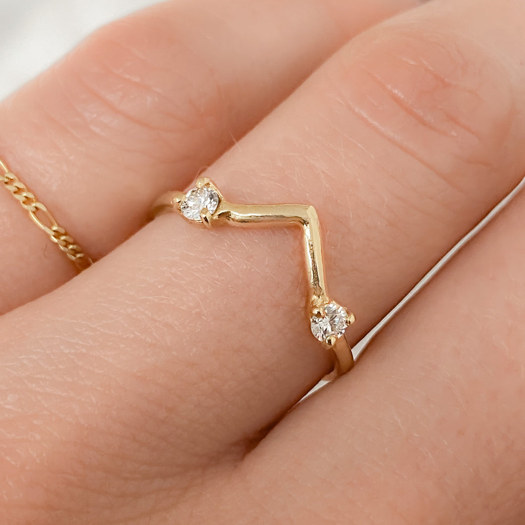 A person's hand wearing a pointed gold band ring with two white diamonds set on it.