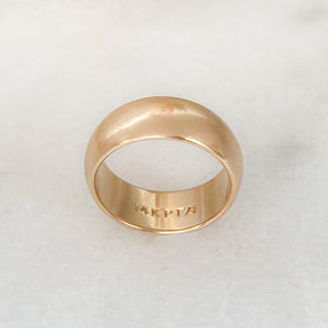 Half dome, yellow gold wedding band lying on its side with inside engraving of "14KPFA" visible