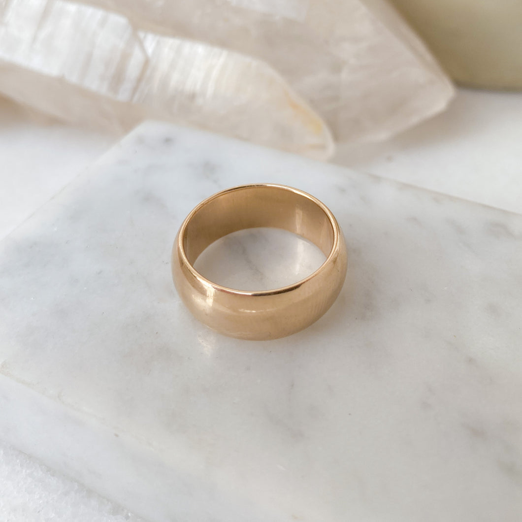 A vintage 14k yellow gold half dome wedding band ring with a polished finish, placed on a white marble surface, with white crystals in the background.