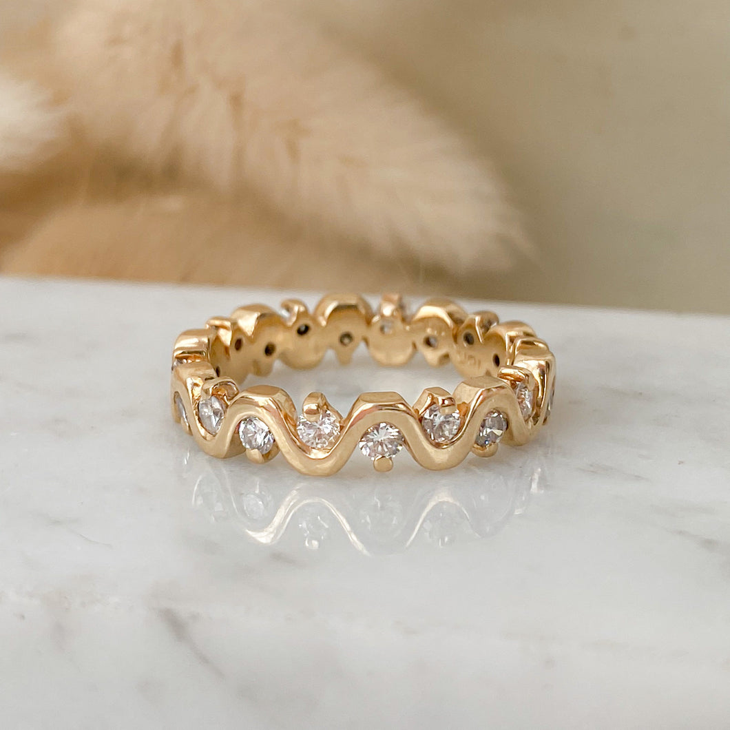 An undulating wave ring of 14k gold with diamonds on marble surface